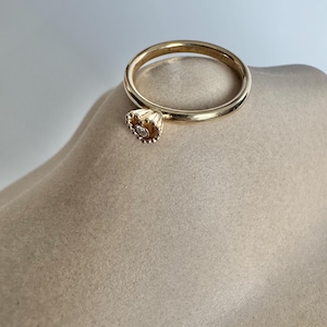 Puede incluir: Un anillo de oro con un pequeño diamante engastado en un delicado diseño festoneado.
