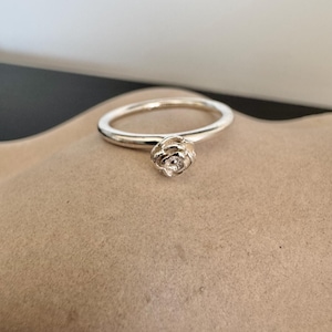 Puede incluir: Un anillo de plata con una pequeña piedra transparente engastada en un diseño en forma de rosa.