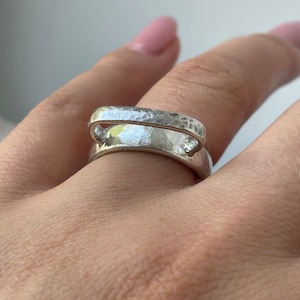Puede incluir: Un anillo de plata con un diseño único, martillado, de banda abierta. El anillo se lleva en un dedo.