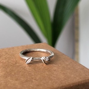Puede incluir: Un anillo de plata con dos acentos en forma de hoja y un pequeño diamante en una de las hojas.