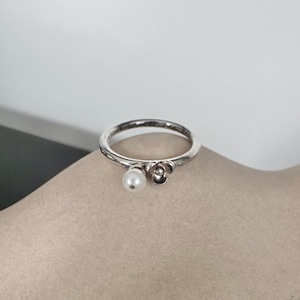 Puede incluir: Un anillo de plata con una perla y un pequeño diseño de flor.