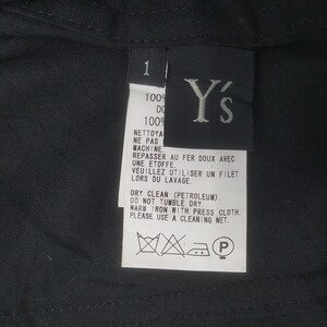 May include: Close-up of a black garment tag with white text and the brand logo "Y's". The tag includes care instructions in English and French, such as "Dry Clean" and "Do Not Tumble Dry".