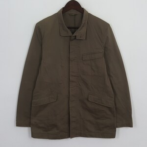 Puede incluir: Chaqueta verde oliva con cuello, dos bolsillos delanteros y cierre de botones. La chaqueta est&aacute; colgada de una percha de madera sobre un fondo blanco. La chaqueta tiene mangas largas.