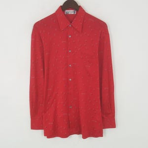 Può includere: Camicia rossa a maniche lunghe con un piccolo motivo ripetuto. La camicia ha una tasca sul petto e un colletto. Il marchio "GIVENCHY" è visibile sull'etichetta. La camicia è appesa a una gruccia di legno.