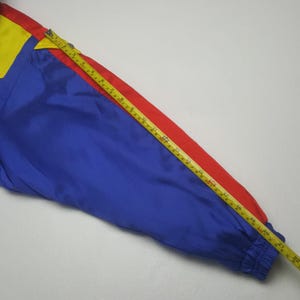 May include: A section of a colorful jacket in primary colors: blue, red, and yellow. A yellow and gold measuring tape is laid across the jacket, showing a measurement of approximately 22 inches.
