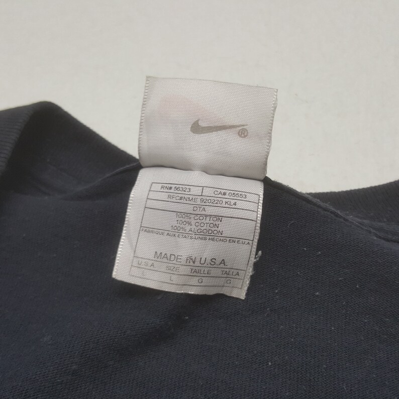 Peut inclure: Un t-shirt noir avec une &eacute;tiquette blanche portant le logo Nike. L'&eacute;tiquette indique que le t-shirt est en 100% coton et fabriqu&eacute; aux &Eacute;tats-Unis. L'&eacute;tiquette comprend &eacute;galement des informations sur la taille.