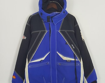 Pode incluir: Casaco azul, preto e branco com capuz e fecho de correr frontal. O casaco apresenta gola alta, vários bolsos e detalhes de costura brancos. As mangas têm painéis pretos com detalhes brancos e um pequeno emblema.