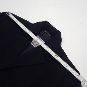 Może przedstawiać: Czarny blazer z miarką na wierzchu. Blazer ma metkę z napisem "TUV SPORT". Miarka pokazuje pomiary w centymetrach. Blazer jest wyprodukowany we Włoszech.