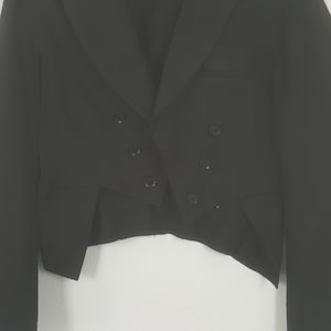 May include: A black formal jacket with a double-breasted front and six buttons. The jacket has a notched lapel and a tailored fit. The sleeves are long, and the jacket is made of a smooth, dark fabric. The jacket is likely for formal events.