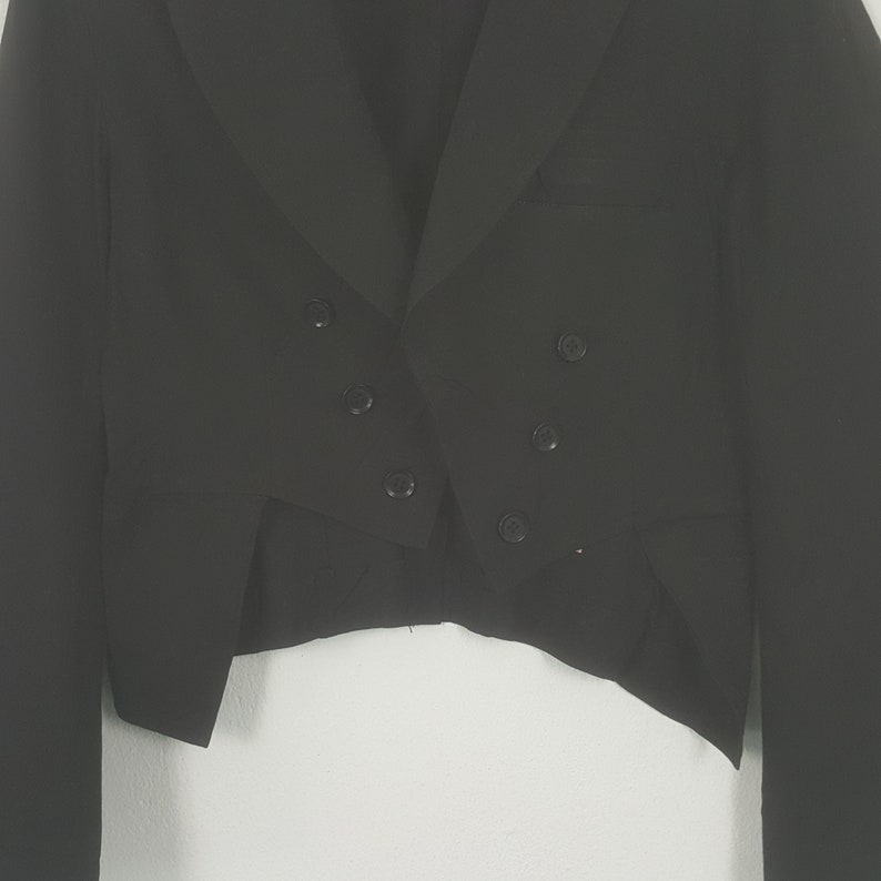 May include: A black formal jacket with a double-breasted front and six buttons. The jacket has a notched lapel and a tailored fit. The sleeves are long, and the jacket is made of a smooth, dark fabric. The jacket is likely for formal events.