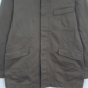 Puede incluir: Chaqueta marr&oacute;n con cuatro bolsillos delanteros. La chaqueta tiene cierre de botones y cuello. La tela parece ser un material duradero, posiblemente lona o sarga. La chaqueta es de color liso y tiene un dise&ntilde;o sencillo y utilitario.
