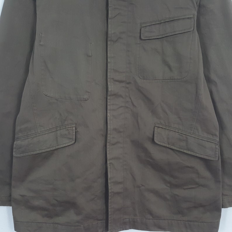 Puede incluir: Chaqueta marr&oacute;n con cuatro bolsillos delanteros. La chaqueta tiene cierre de botones y cuello. La tela parece ser un material duradero, posiblemente lona o sarga. La chaqueta es de color liso y tiene un dise&ntilde;o sencillo y utilitario.
