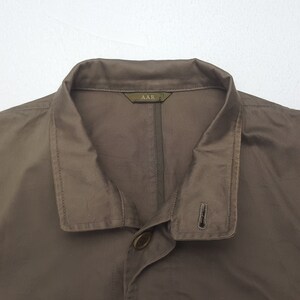Puede incluir: Primer plano de una chaqueta marr&oacute;n con cuello y cierre de un solo bot&oacute;n. La chaqueta tiene una etiqueta que dice "AAR". La tela parece ser ligera. La chaqueta es de color liso.