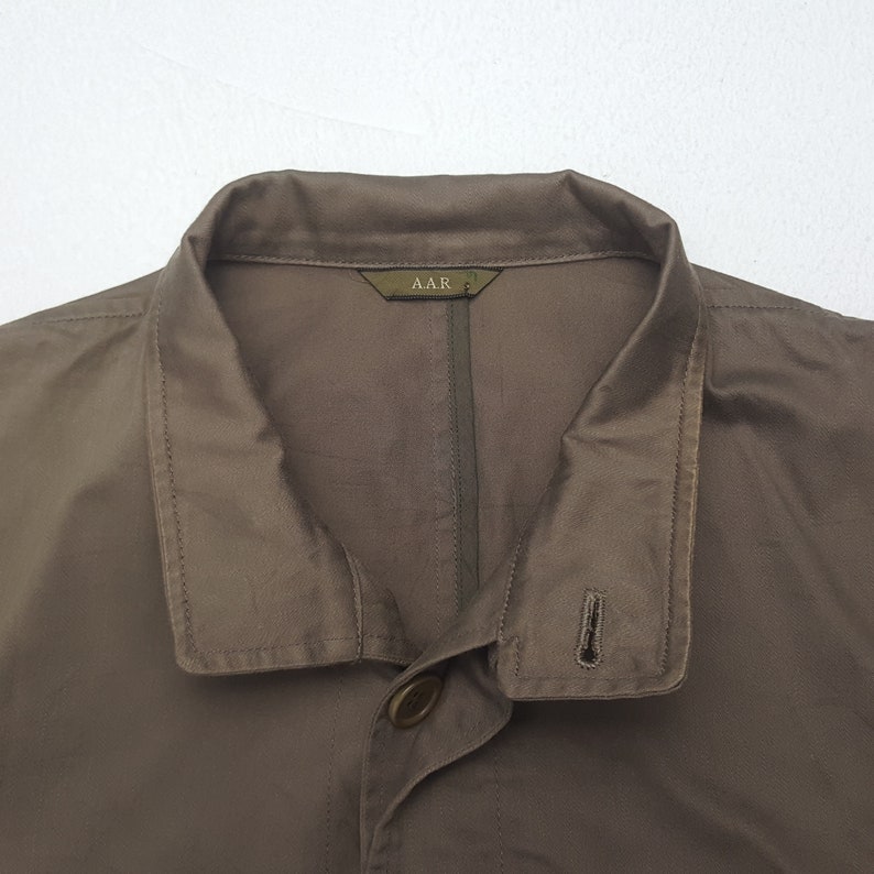 Puede incluir: Primer plano de una chaqueta marr&oacute;n con cuello y cierre de un solo bot&oacute;n. La chaqueta tiene una etiqueta que dice "AAR". La tela parece ser ligera. La chaqueta es de color liso.