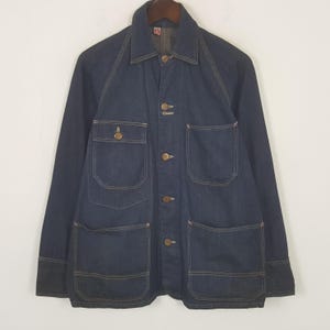 May include: A dark blue denim jacket with four front pockets and button fastenings. The jacket features a collared neckline and long sleeves. The stitching is a contrasting light brown colour.
