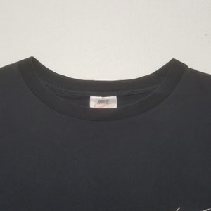 Peut inclure: T-shirt noir &agrave; col rond avec le logo Nike sur l'&eacute;tiquette. Le t-shirt est uni et a un design simple. Le logo Nike est blanc avec un swoosh rouge.