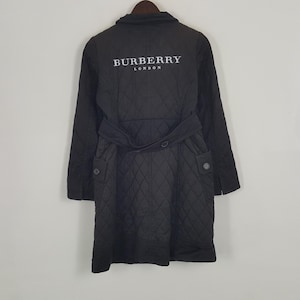 Op de afbeelding: Zwarte gewatteerde jas met riem en knoopdetails. De jas heeft de tekst "BURBERRY LONDON" in het wit op de bovenrug. De jas heeft een ruitpatroon over de hele stof.