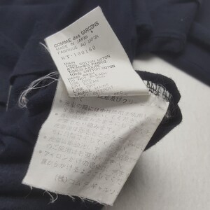 K&ouml;nnte beinhalten: Nahaufnahme eines marineblauen Kleidungsst&uuml;cketiketts mit wei&szlig;em Text. Das Etikett lautet "COMME des GARCONS MADE IN JAPAN FABRIQUE AU JAPON" und enth&auml;lt Pflegehinweise in Englisch und Japanisch. Das Kleidungsst&uuml;ck besteht aus 100 % Baumwolle.