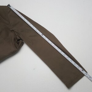 Puede incluir: Una manga de chaqueta marr&oacute;n se mide con una cinta m&eacute;trica. La manga es de color marr&oacute;n liso y apagado. La cinta m&eacute;trica muestra una longitud de aproximadamente 66 cm.