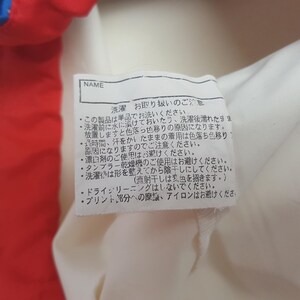 Puede incluir: Primer plano de una etiqueta de tela blanca con texto japon&eacute;s y la palabra "NAME" en la parte superior. La etiqueta est&aacute; adherida a una prenda roja y blanca. El texto proporciona instrucciones de lavado.