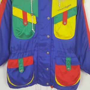 May include: A colorful vintage jacket with a blue base, featuring red, yellow, and green accents. The jacket has multiple pockets, a drawstring waist, and the brand name "courr&egrave;ges" printed on the upper right.