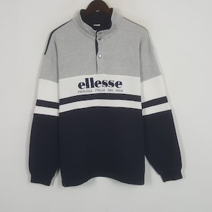May include: A gray, white, and navy blue sweatshirt with the brand name "ellesse" printed across the chest. The sweatshirt has a button-up collar and long sleeves. The text "PERUGIA ITALIA DAL 1959" is printed below the brand name.