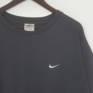 Peut inclure: T-shirt noir &agrave; col rond avec un petit logo Nike blanc sur la poitrine gauche. Le t-shirt est suspendu &agrave; un cintre en bois sur fond blanc. Le logo Nike est brod&eacute;.