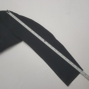 May include: A black garment sleeve is measured with a yellow and white measuring tape. The sleeve is approximately 22 inches long. The background is a plain white surface.