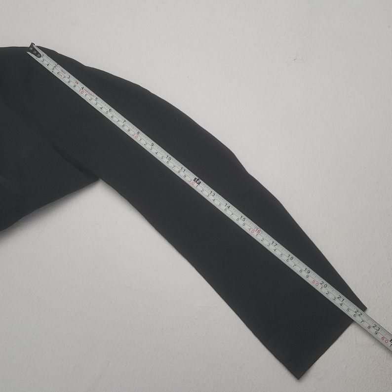 May include: A black garment sleeve is measured with a yellow and white measuring tape. The sleeve is approximately 22 inches long. The background is a plain white surface.