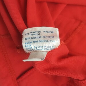 May include: Close-up of a red fabric with a white tag. The tag has text indicating the fabric composition: 87% Triacetate, 13% Polyester. Washing instructions are also printed on the tag.