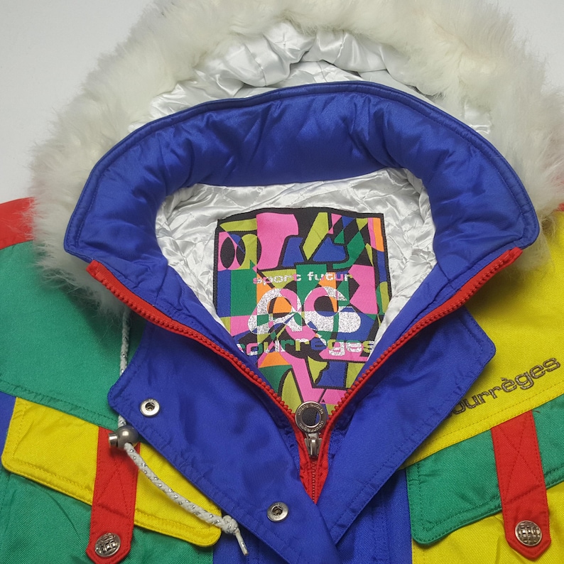 May include: A colorful vintage ski jacket with a white faux fur-lined hood. The jacket features a blue collar, a red zipper, and panels of yellow, green, and red. The label inside reads "Courr&egrave;ges".