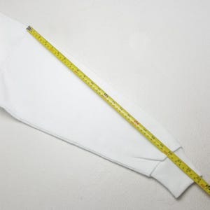 Może przedstawiać: Biały rękaw bluzy z ż&oacute;łtą miarką na wierzchu. Miarka pokazuje pomiary w centymetrach, a rękaw ma około 58 cm długości.