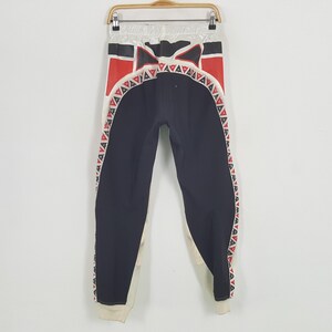 Peut inclure: Pantalon de sport noir et blanc avec des motifs g&eacute;om&eacute;triques rouges et blancs. Le pantalon a une taille et des poignets blancs. Le motif comprend des triangles rouges et un motif noir et rouge sur le dessus.