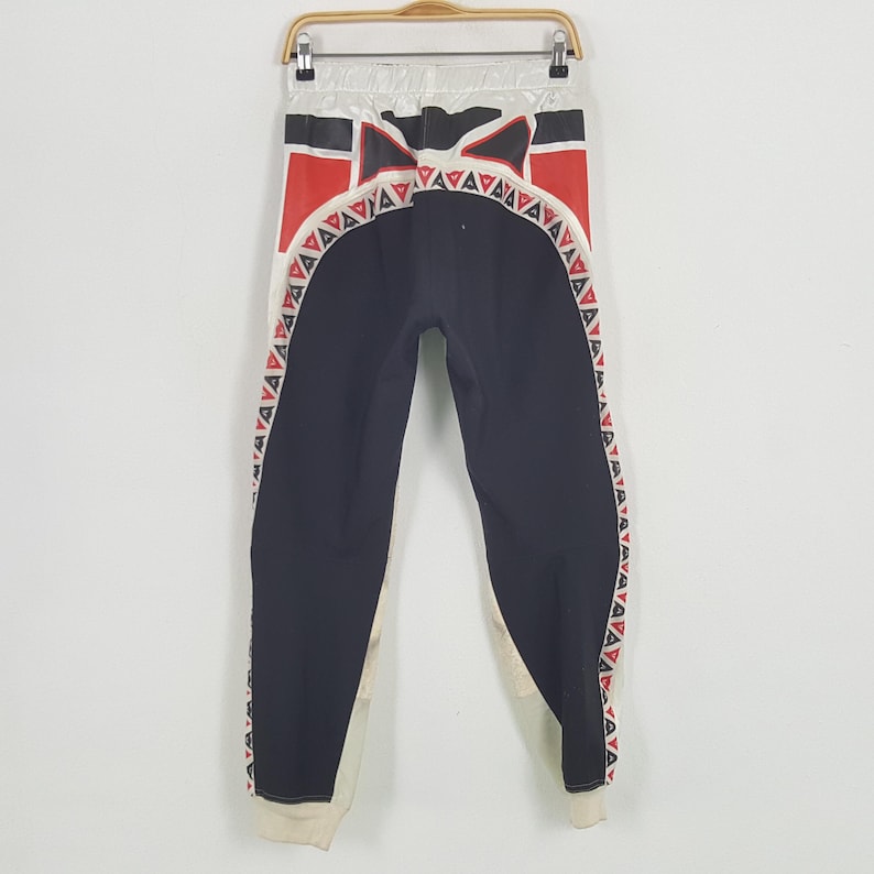 Peut inclure: Pantalon de sport noir et blanc avec des motifs g&eacute;om&eacute;triques rouges et blancs. Le pantalon a une taille et des poignets blancs. Le motif comprend des triangles rouges et un motif noir et rouge sur le dessus.