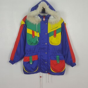 May include: A vintage, color-blocked winter coat with a blue base, red sleeves, and green and yellow pockets. The coat features a fur-lined hood and the brand name "courr&egrave;ges" in yellow. It has a drawstring waist and button closures.