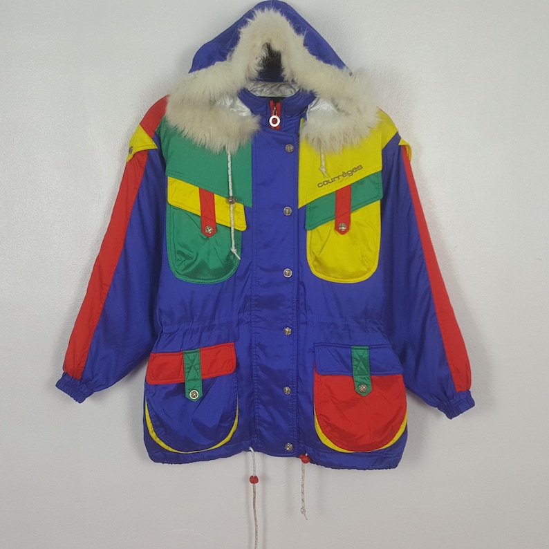 May include: A vintage, color-blocked winter coat with a blue base, red sleeves, and green and yellow pockets. The coat features a fur-lined hood and the brand name "courr&egrave;ges" in yellow. It has a drawstring waist and button closures.