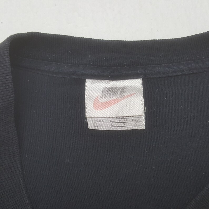Peut inclure: T-shirt noir avec une &eacute;tiquette Nike. L'&eacute;tiquette est rectangulaire avec le logo Nike en rouge et blanc. L'&eacute;tiquette indique &eacute;galement la taille, qui est grande.