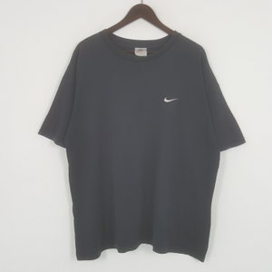 Peut inclure: Un t-shirt gris fonc&eacute; avec un petit logo Nike blanc sur la poitrine gauche. Le t-shirt a des manches courtes et un col rond. Le t-shirt est suspendu &agrave; un cintre en bois.