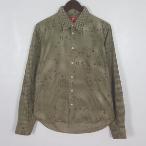 May include: A long-sleeved button-down shirt in a green and brown checkered pattern with a small red logo on the chest. The shirt has a classic collar and buttoned cuffs. The shirt is hanging on a wooden hanger.