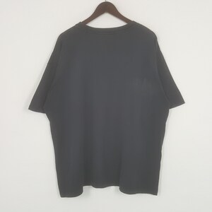 Peut inclure: T-shirt noir &agrave; col rond, suspendu &agrave; un cintre en bois. Le t-shirt a des manches courtes et est fait d'une mati&egrave;re douce. Le v&ecirc;tement est de couleur unie et semble neuf.