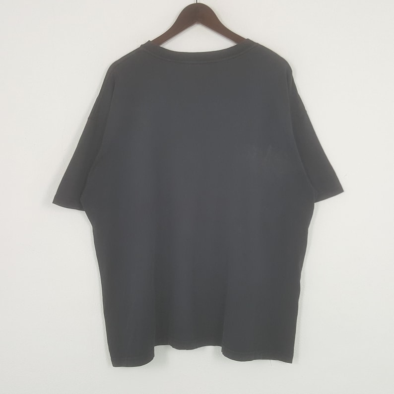 Peut inclure: T-shirt noir &agrave; col rond, suspendu &agrave; un cintre en bois. Le t-shirt a des manches courtes et est fait d'une mati&egrave;re douce. Le v&ecirc;tement est de couleur unie et semble neuf.