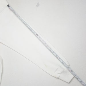 May include: A white long-sleeved sweatshirt with a tape measure laid across the sleeve. The tape measure shows measurements in inches, with the sleeve measuring approximately 28 inches in length. The sweatshirt is on a white background.