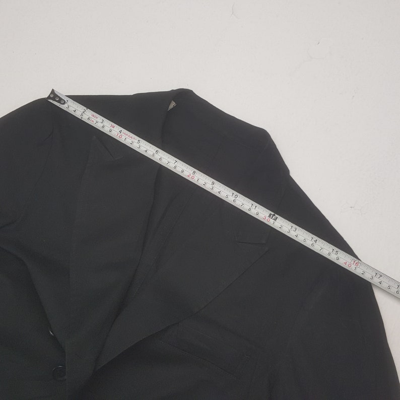 May include: A black blazer with a single-button closure, a notched lapel, and a chest pocket. A measuring tape shows the blazer's length is approximately 17 inches. The blazer is made of a smooth, solid fabric.