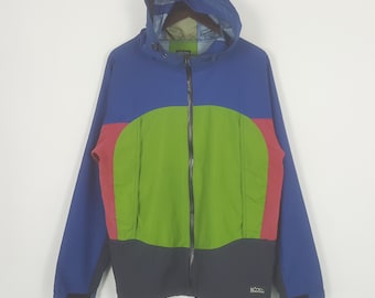 Könnte beinhalten: Eine mehrfarbige Kapuzenjacke in Blau, Rot, Grün und Schwarz. Die Jacke hat einen durchgehenden Reißverschluss, eine Kapuze und ein kleines Logo unten rechts. Die Jacke ist aus leichtem Material gefertigt und eignet sich für Outdoor-Aktivitäten.
