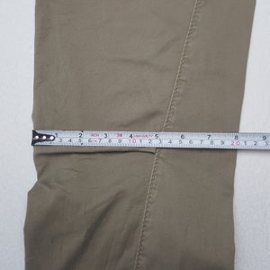May include: Close-up of tan-colored pants with a measuring tape showing a width of approximately 8 inches. The tape measure is marked in inches and centimeters, indicating the garment's dimensions.
