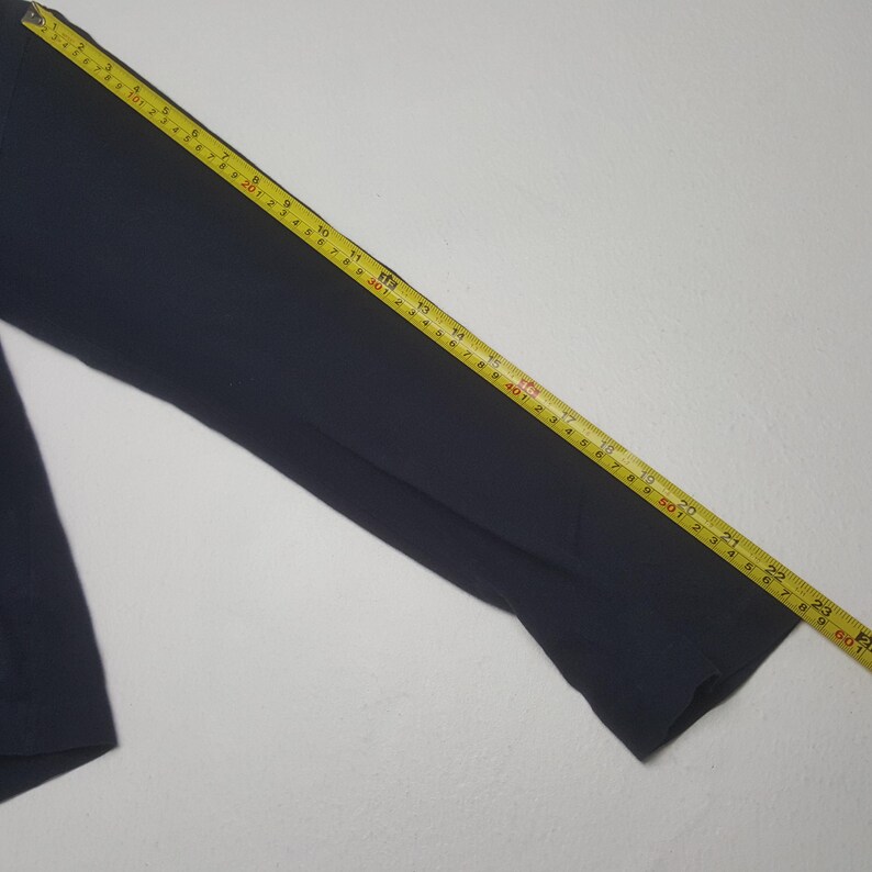 K&ouml;nnte beinhalten: Ein marineblaues Langarmhemd mit einem gelben Ma&szlig;band auf dem &Auml;rmel. Das Band zeigt Messungen in Zentimetern, wobei die &Auml;rmell&auml;nge etwa 58 cm betr&auml;gt.
