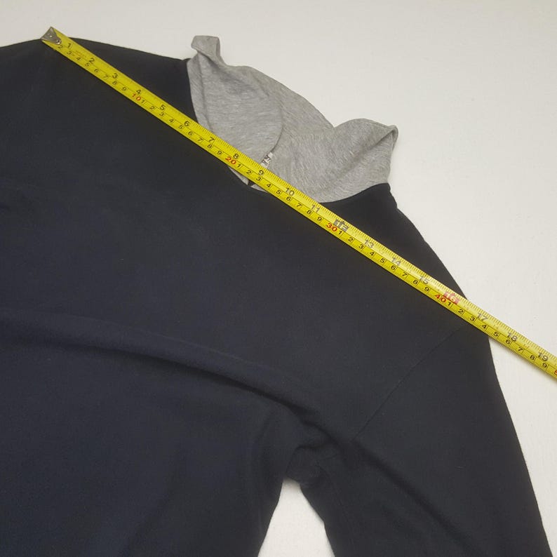 K&ouml;nnte beinhalten: Ein schwarzes Langarmshirt mit grauem Rundhalsausschnitt. Ein gelbes Ma&szlig;band liegt &uuml;ber dem Shirt und zeigt Messungen in Zentimetern an. Das Shirt ist aus weichem Material.