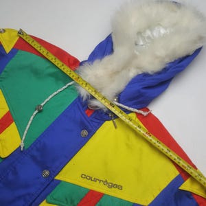 May include: A colorful vintage winter jacket with a fur-lined hood. The jacket features a patchwork design in red, yellow, green, and blue. The brand name "courr&egrave;ges" is visible on the front. A measuring tape is laid across the jacket.