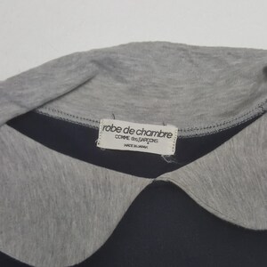 K&ouml;nnte beinhalten: Nahaufnahme eines marineblauen und grauen Hemdes mit Kragen. Der Kragen ist grau, darunter ein marineblaues Band. Ein Etikett lautet "robe de chambre COMME des GARCONS MADE IN JAPAN."