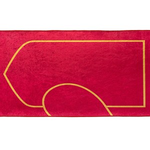 May include: A red prayer rug with a gold geometric design and cream-colored fringe. The rug features a central rectangular shape with a curved design, suitable for prayer and meditation.